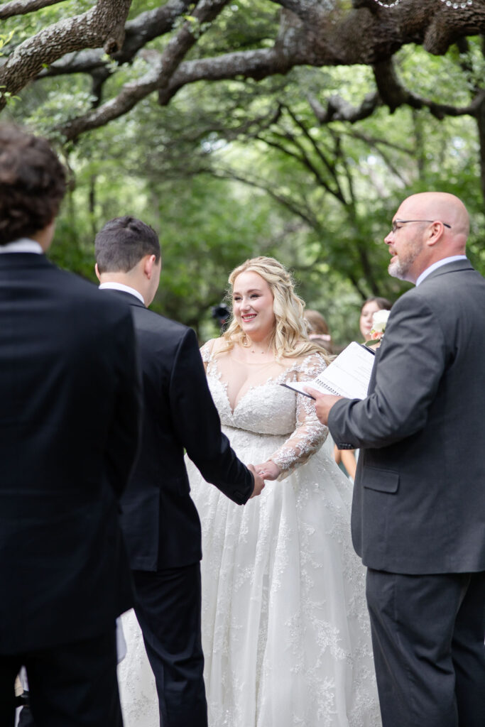 Outdoor wedding ceremony at Trickle Creek Ranch in Weatherford, Texas featuring a stone aisle, mature live oak trees, and a romantic natural setting.